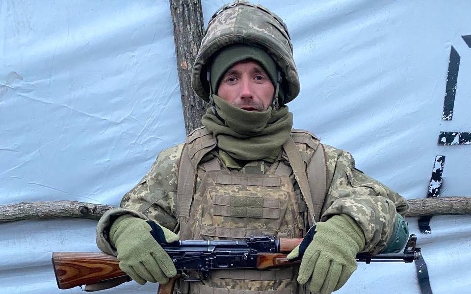 Żołnierz w mundurze z bronią, stojący w obozie.