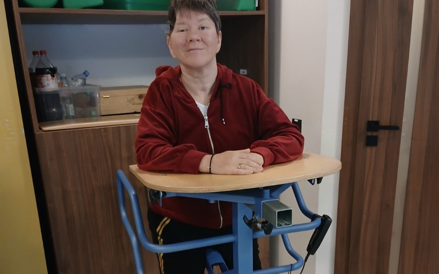 
        Kobieta uśmiechająca się przy stelażu do chodzenia.
    