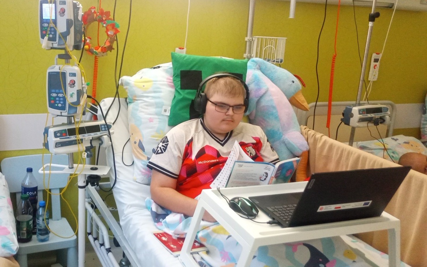 
        Chłopiec w szpitalu, czyta książkę i korzysta z laptopa.
    