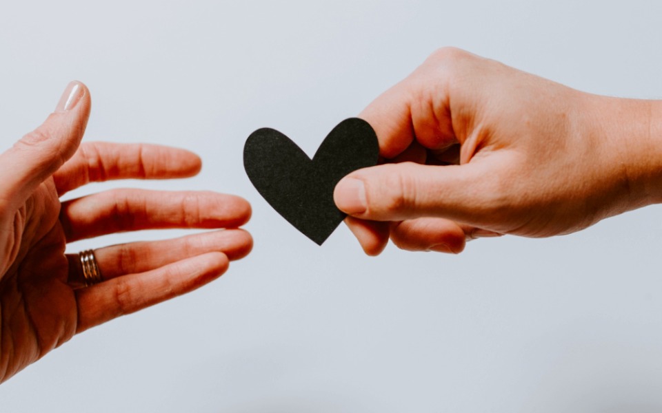
        Dwie ręce sięgające po czarny papierowy serce, symbolizujące miłość.
    