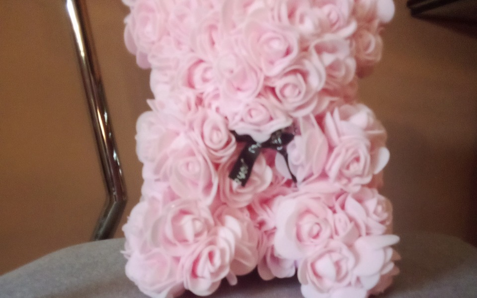 
        Różowa figurka z kwiatów, przypominająca misia, ozdobiona czarną wstążką.
    