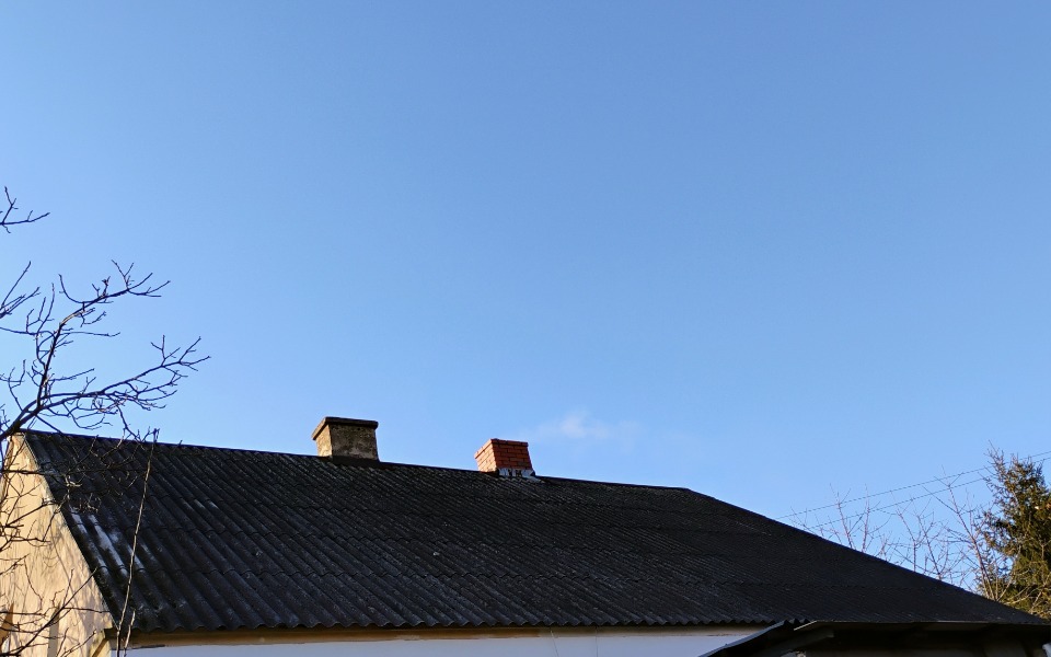 
        Dach domu pod błękitnym niebem, spokojny widok.
    