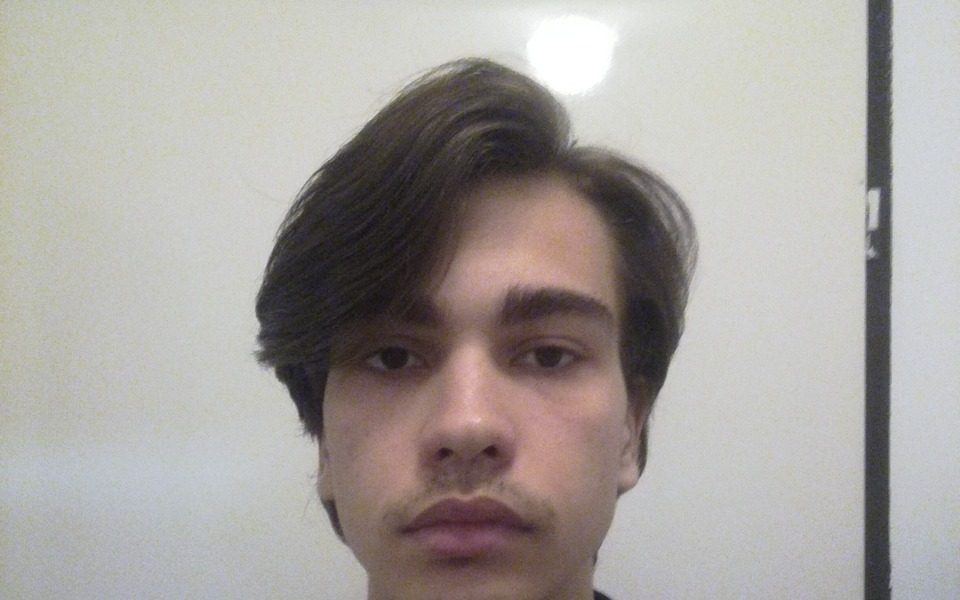 
        Młody mężczyzna patrzący w kamerę, z długimi włosami.
    