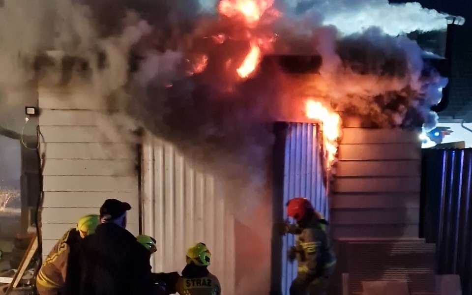 
        Strażacy gaszący pożar w budynku, otoczeni dymem.
    