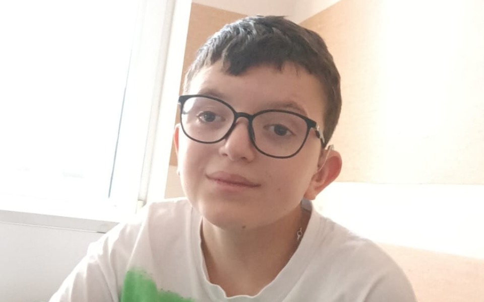 
        Chłopiec w okularach, siedzący przy oknie.
    