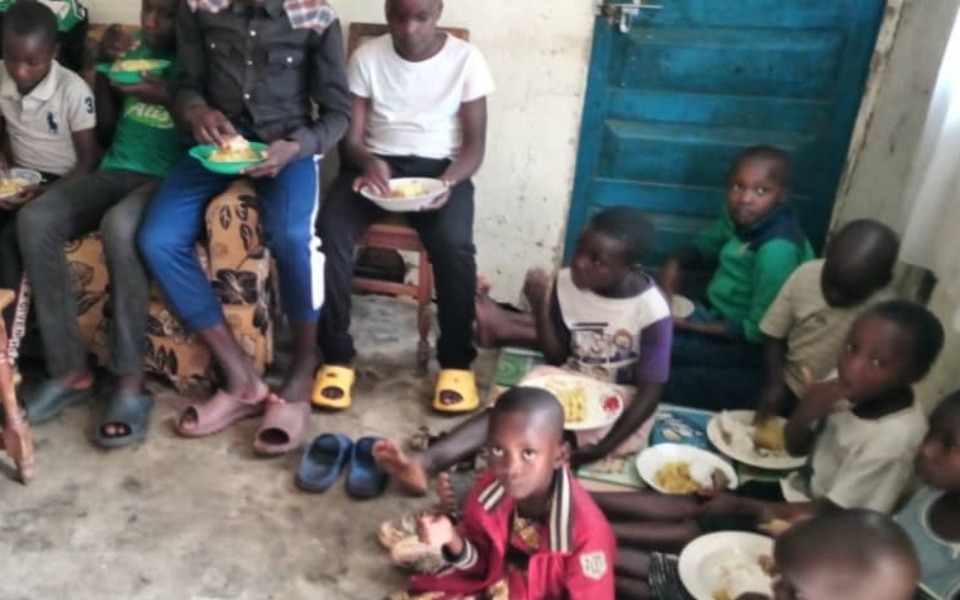 
        Grupa dzieci jedzących posiłek w skromnym pomieszczeniu.
    