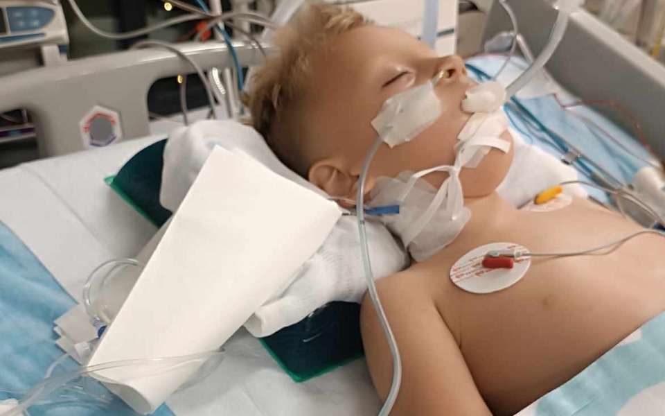 
        Dziecko na łóżku szpitalnym z podłączonymi urządzeniami medycznymi.
    