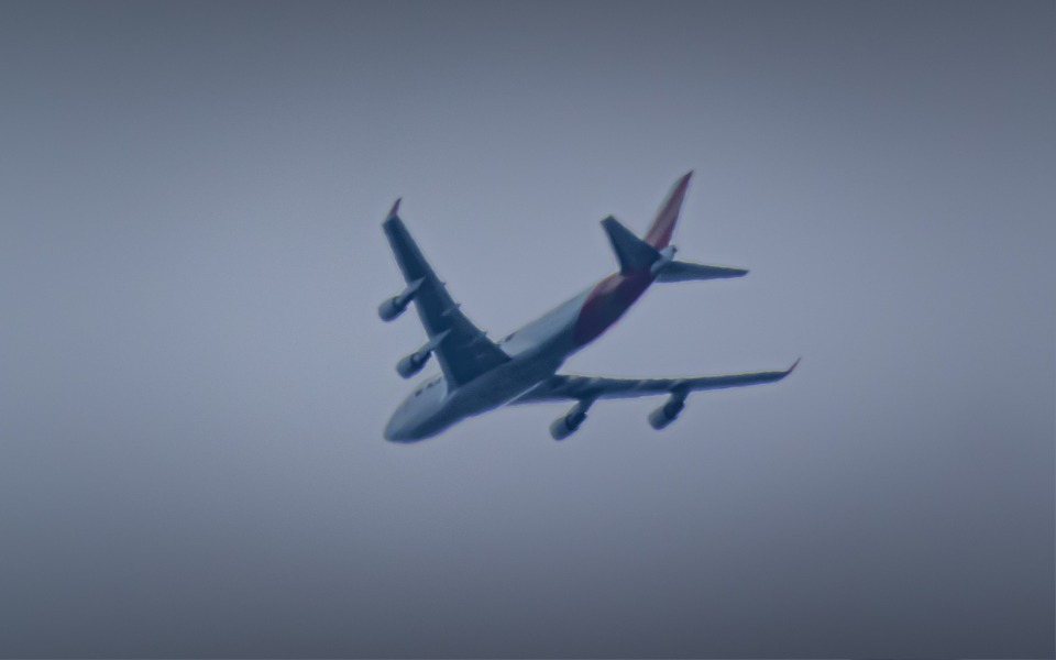 
        Samolot w locie, widoczny na szarym niebie.
    