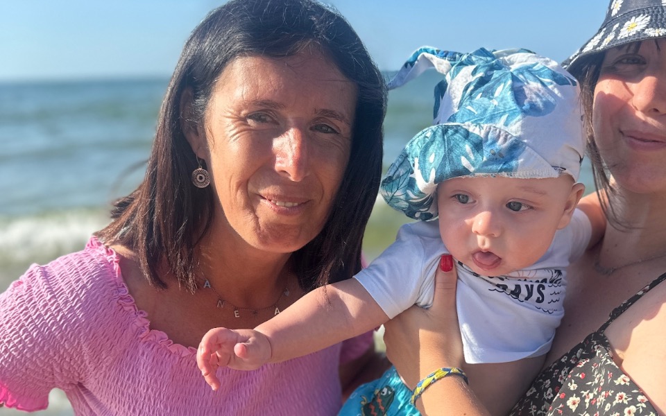 
        Rodzina na plaży, matka trzyma dziecko w kapeluszu.
    