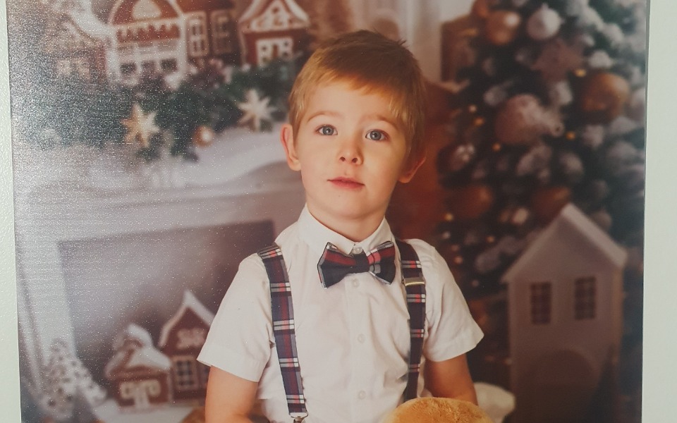 
        Chłopiec w eleganckim stroju z pluszowym misiem, w świątecznym otoczeniu.
    