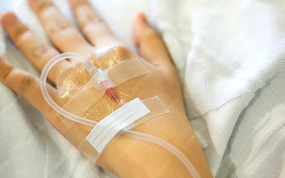 
        Ręka pacjenta z wkłuciem dożylanym na tle szpitalnej pościeli.
    