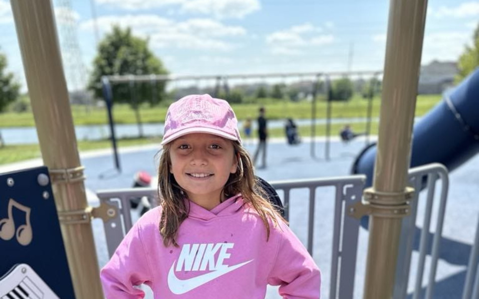 
        Dziewczynka w różowej bluzie na placu zabaw.
    