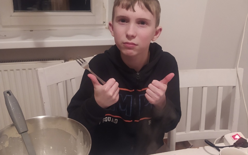 
        Chłopiec z widocznym uśmiechem, trzymający widelec i pokazujący kciuki w górę.
    