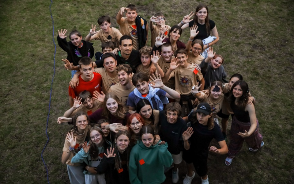 
        Grupa młodych ludzi pozująca do zdjęcia na trawie, uśmiechnięta i radosna.
    