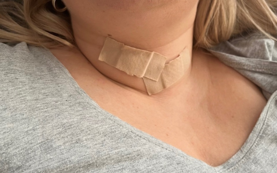 
        Osoba z opatrunkiem na szyi, odpoczywa w domu.
    