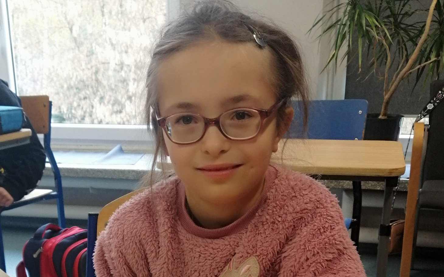 
        Dziewczynka w okularach, uśmiechająca się do kamery.
    