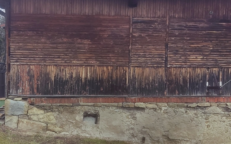 
        Zniszczona drewniana ściana budynku, z widocznymi śladami pożaru.
    