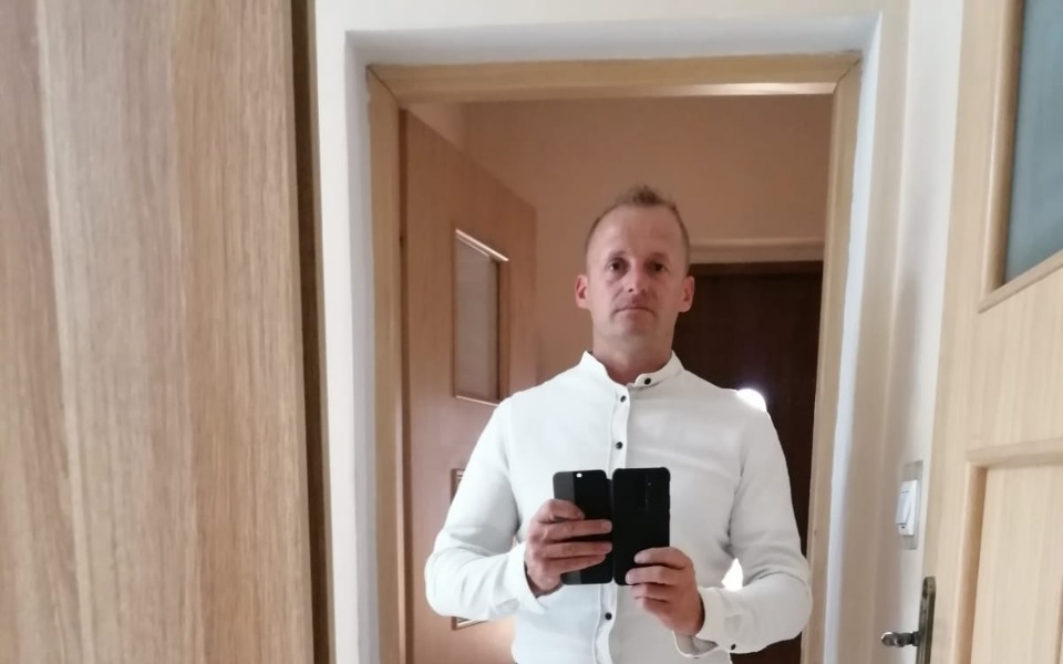 
        Mężczyzna w białej koszuli, trzymający dwa telefony w lustrze.
    