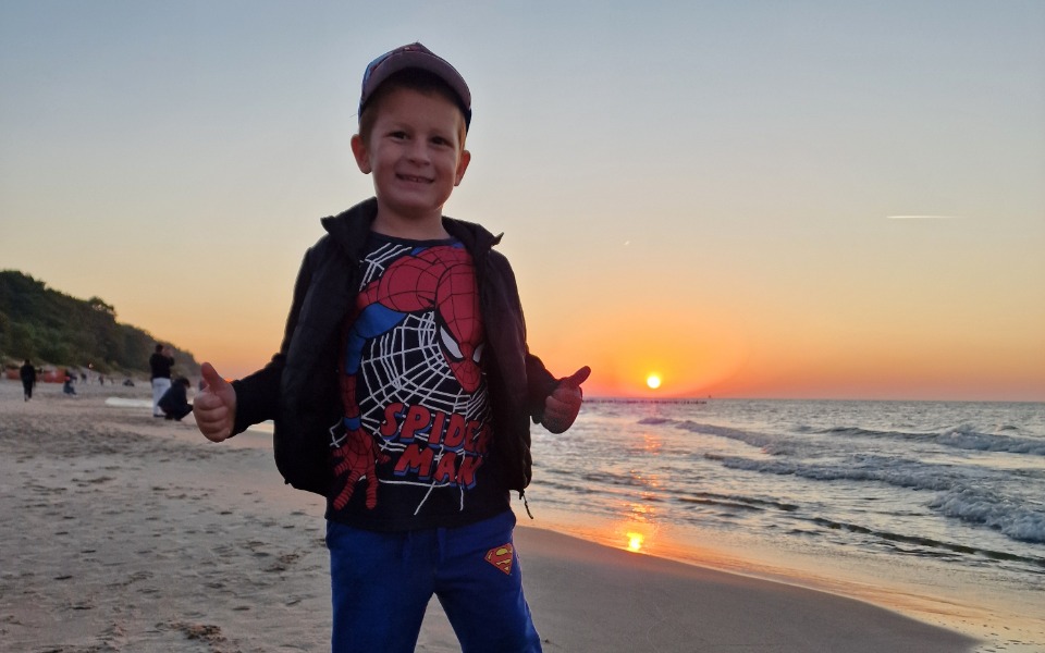 
        Chłopiec na plaży, cieszący się zachodem słońca.
    