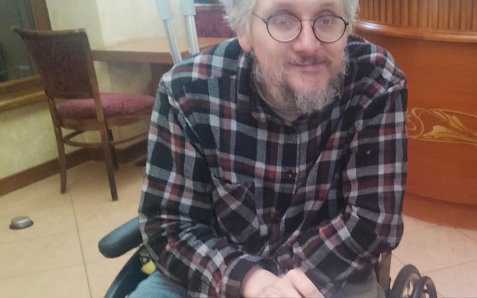 
        Mężczyzna w okularach, siedzący na wózku inwalidzkim.
    