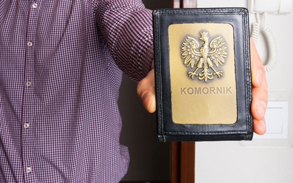 
        Osoba trzymająca legitymację komornika z orłem na okładce.
    