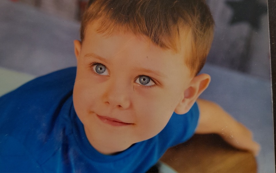 
        Chłopiec z niebieskimi oczami, uśmiechający się do kamery.
    