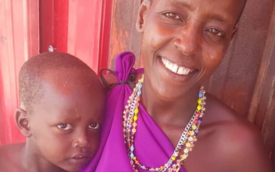 
        Uśmiechnięta kobieta z dzieckiem na rękach, w tradycyjnym stroju.
    