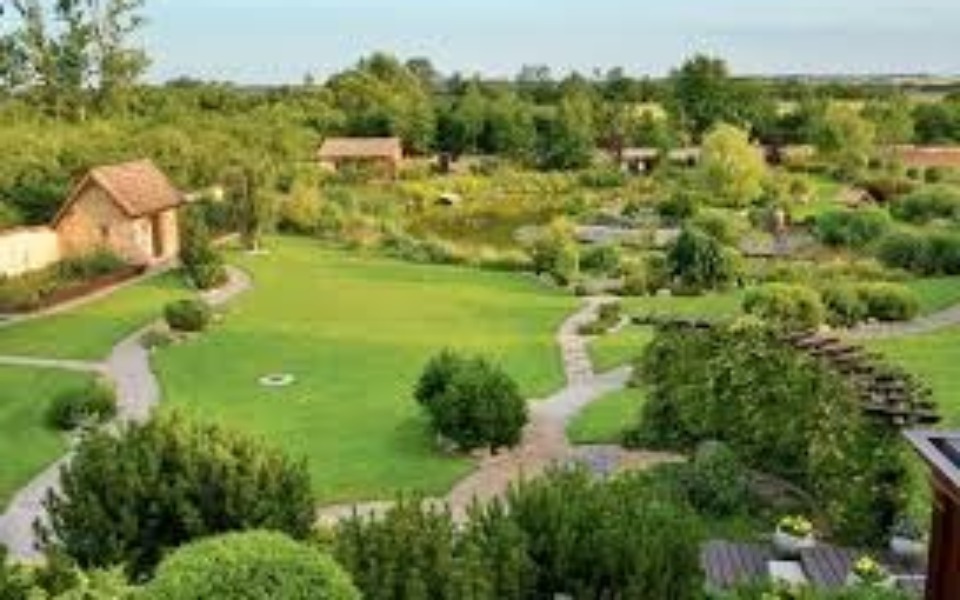 
        Widok na zadbany ogród z alejkami i roślinnością.
    