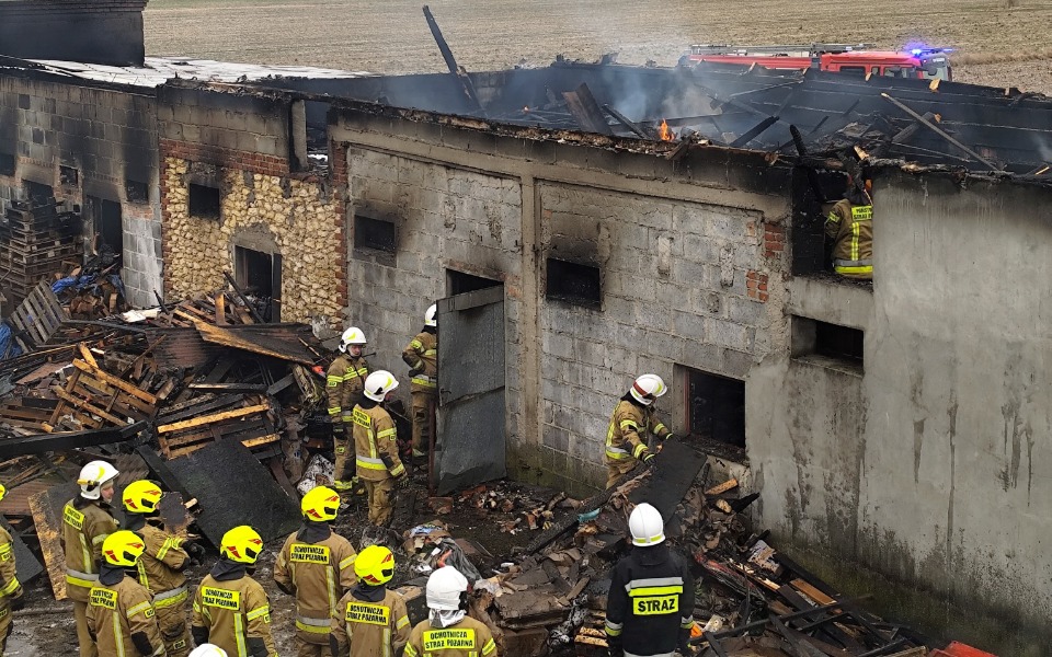 
        Strażacy gaszą pożar budynku, dym unosi się w powietrzu.
    