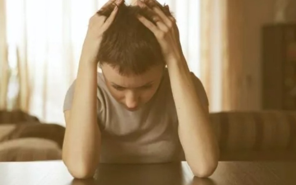 
        Zmartwiona kobieta trzymająca się za głowę w domowym wnętrzu.
    