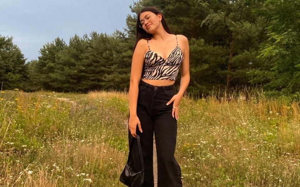 
        Młoda kobieta w modnej bluzce na tle zielonej łąki.
    