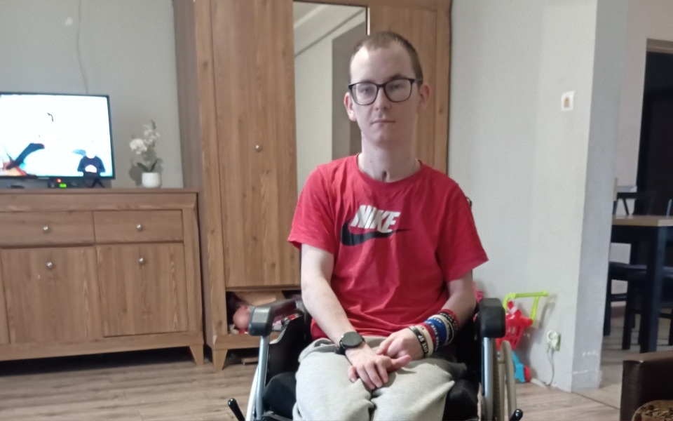 
        Młody mężczyzna na wózku inwalidzkim, siedzący w pokoju.
    