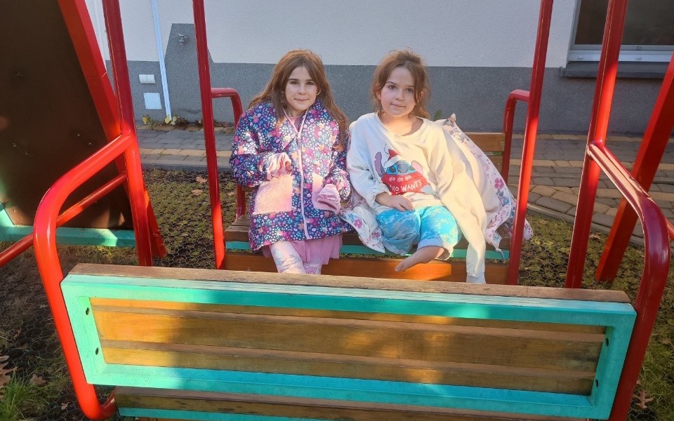 
        Dwie dziewczynki bawiące się na huśtawce.
    