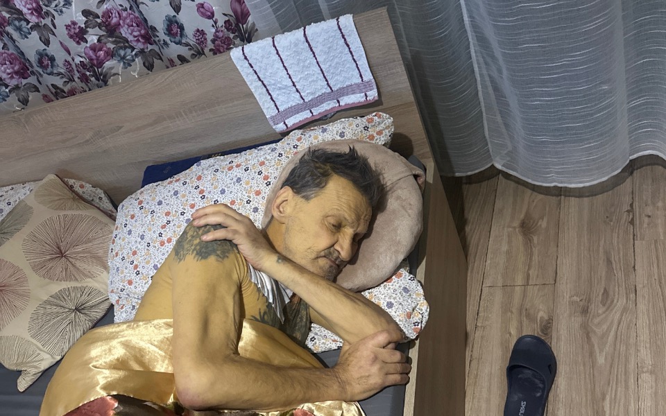 
        Mężczyzna leżący w łóżku, przykryty kocem.
    