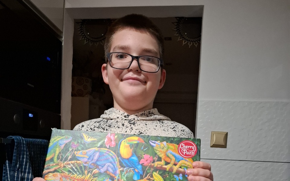 
        Chłopiec trzymający kolorowy obrazek z motywem zwierząt.
    