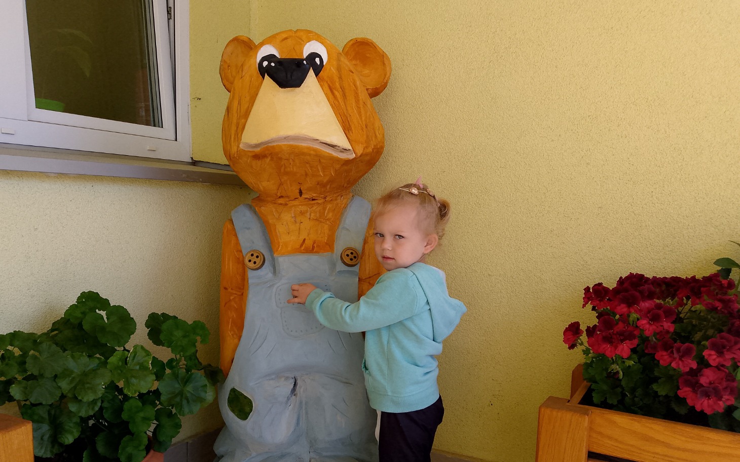 
        Dziewczynka przy drewnianej rzeźbie misia.
    
