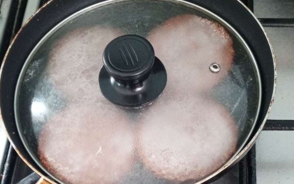 
        Gotujące się kotlety na patelni pod przykrywką.
    