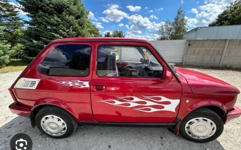 
        Czerwony samochód z białymi płomieniami na boku, na tle nieba.
    