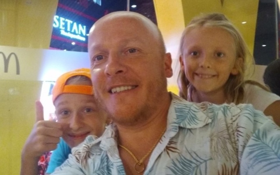 
        Rodzinne selfie z uśmiechniętymi dziećmi i dorosłym w tle.
    