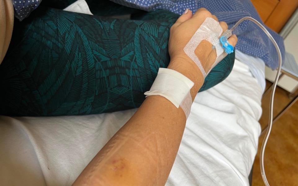 
        Ręka pacjenta z wenflonem, leżąca na łóżku szpitalnym.
    