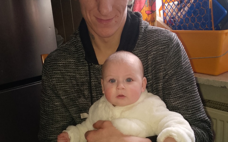 
        Mężczyzna trzymający niemowlę w białym ubranku, oboje patrzą w obiektyw.
    