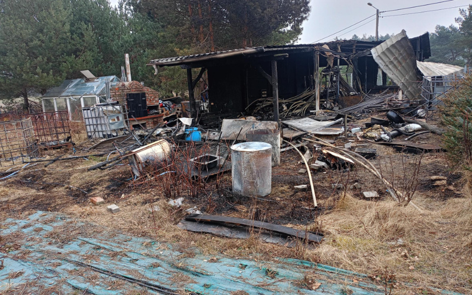 
        Zniszczony budynek z resztkami po pożarze w otoczeniu przyrody.
    