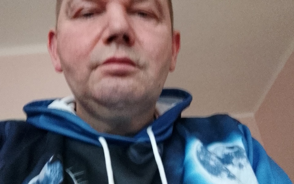 
        Mężczyzna w bluzie z kosmicznym motywem, patrzący w obiektyw.
    