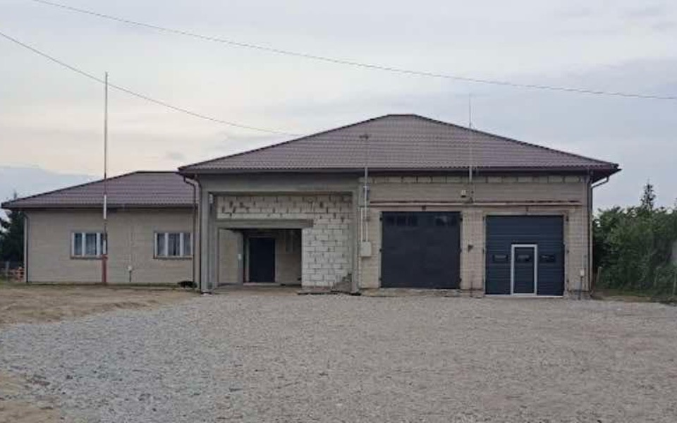 
        Widok na budynek z szarym dachem, otoczony terenem.
    