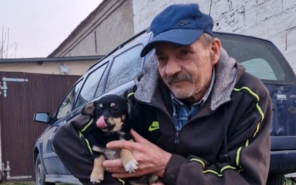 
        Mężczyzna trzymający małego psa, uśmiechający się.
    