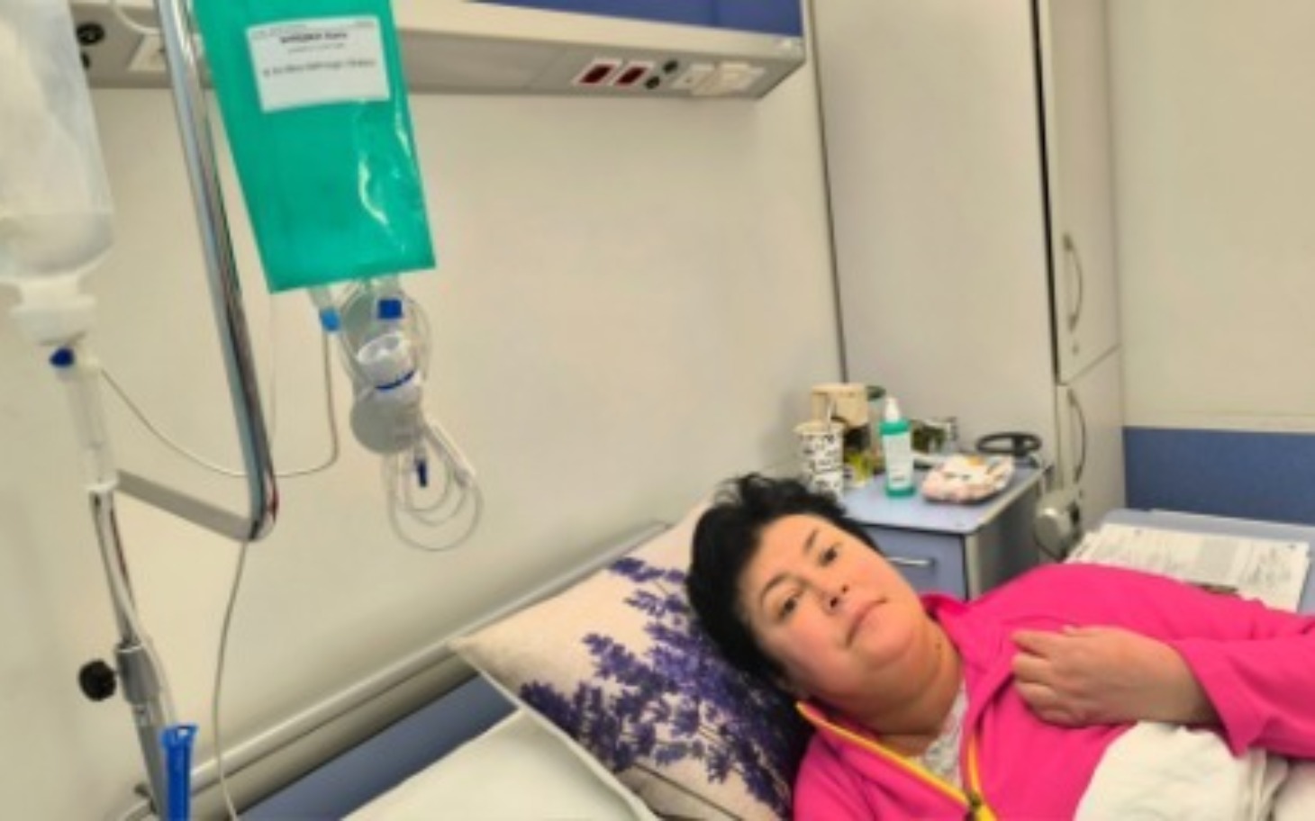 
        Kobieta w szpitalu, z kroplówką i zmartwionym wyrazem twarzy.
    