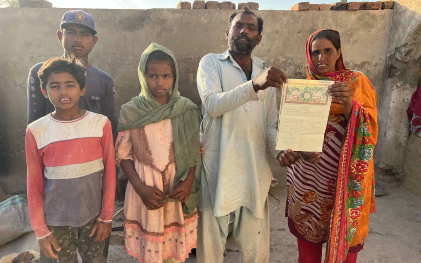 
        Rodzina trzymająca dokument, stojąca na tle zniszczonego budynku.
    