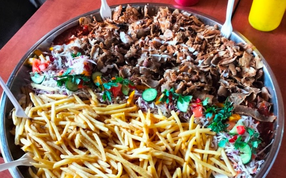 
        Duża taca z jedzeniem, w tym frytkami i mięsem, podana w restauracji.
    