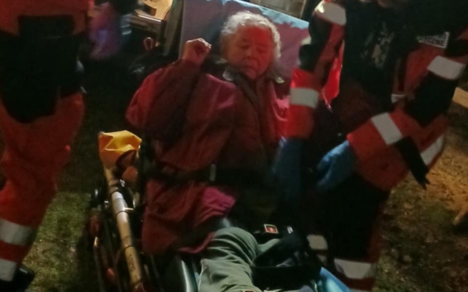 
        Starsza kobieta na noszach, otoczona przez ratowników medycznych.
    