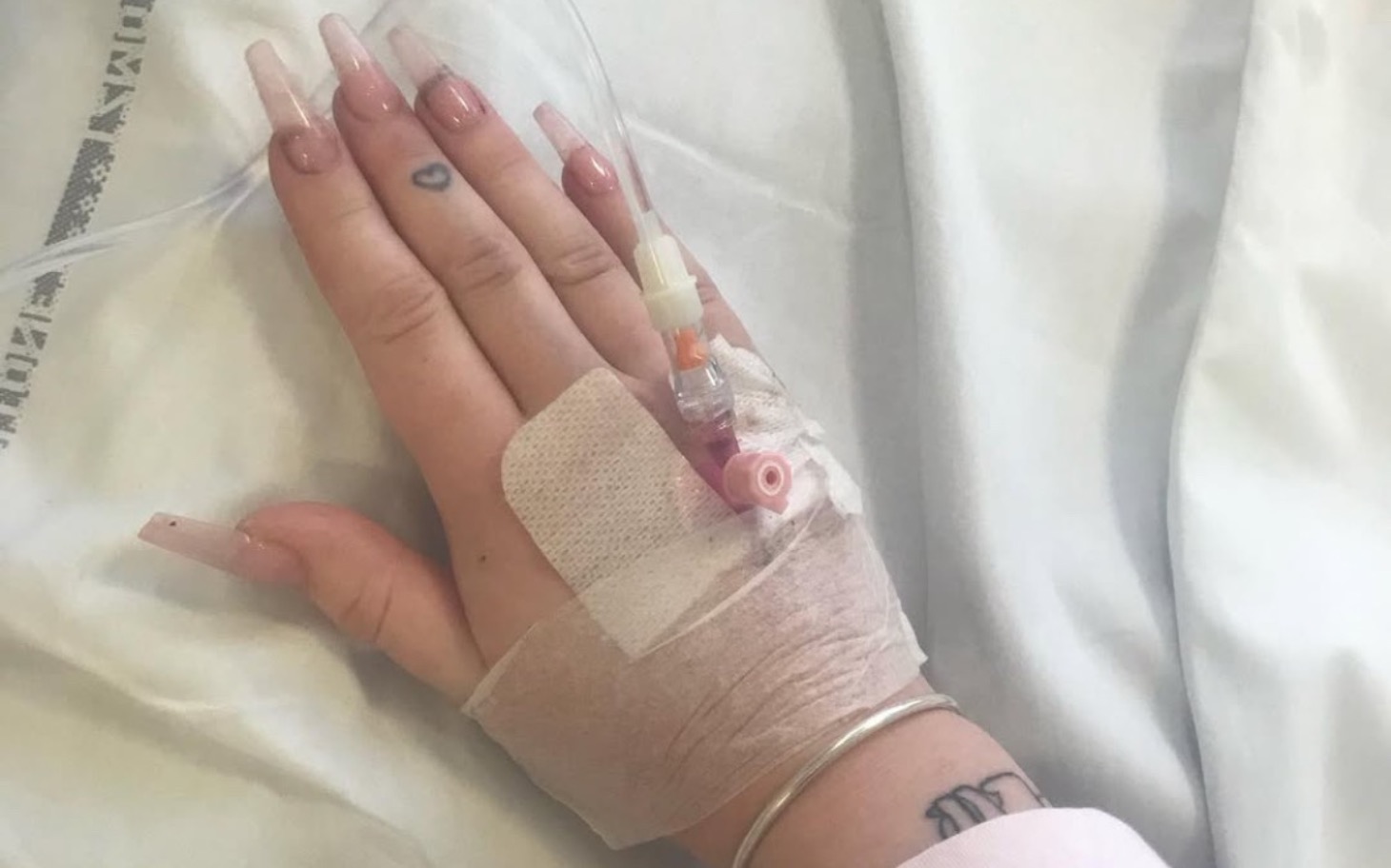 
        Ręka z wenflonem w szpitalu, z ozdobnymi paznokciami i tatuażem.
    